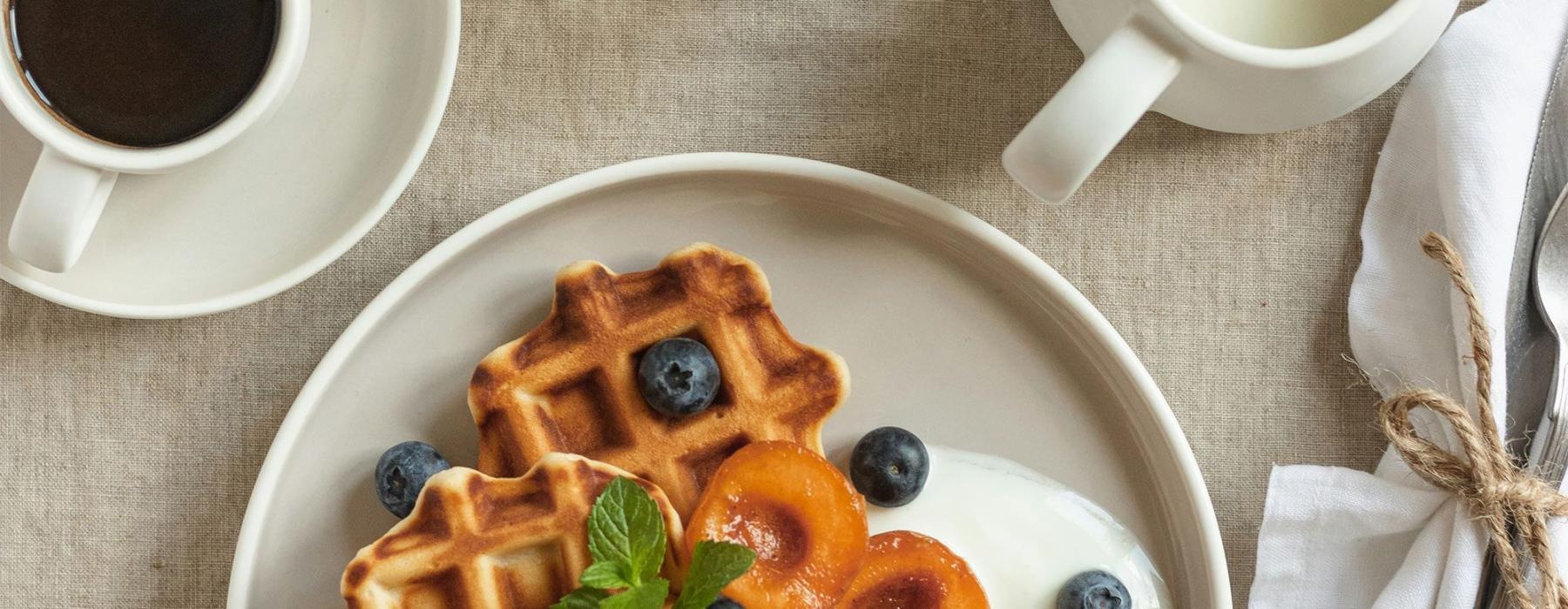 a plate of blueberries and waffles and a cup of coffee