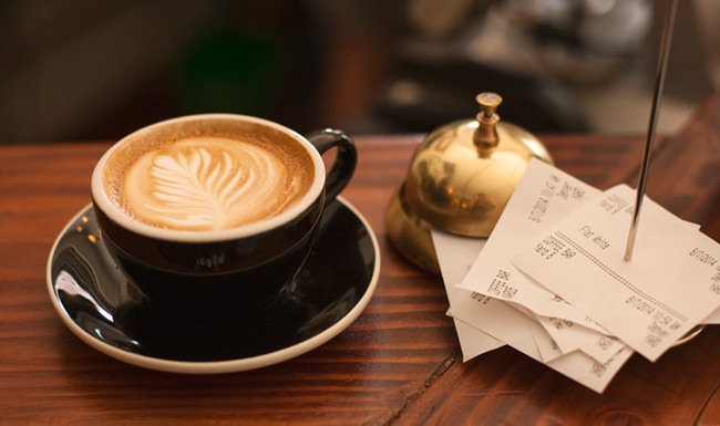 cup of coffee, bell and stack of receipts on a table